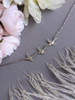 Silver trio of birds bracelet on a gray surface with pink flowers and feathers.