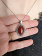 Hand holding a Blood Red Agate Crystal Necklace - Silver Flourish Pendant Setting against a neutral background.