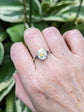 Hand wearing a Pink Rose Cameo Ring - Sterling Silver Adjustable Band  against a green leafy background