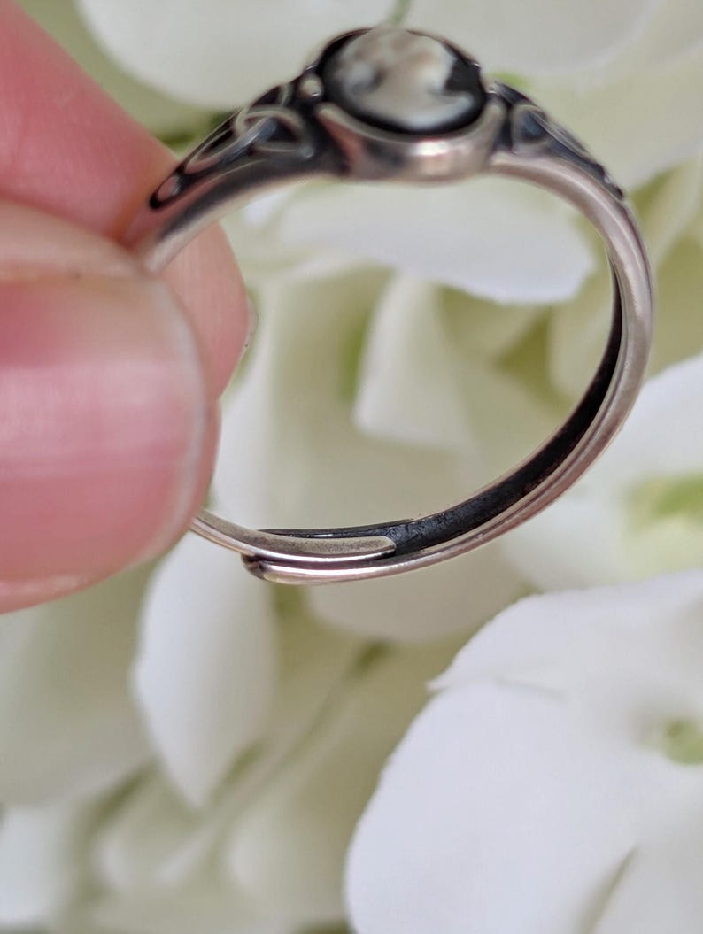Side view of a 925 Sterling Silver Celtic Knot Cameo Ring - Heritage Style Jewelry with an ivory on black cameo on a white floral background