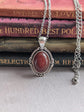 Blood Red Agate Crystal Necklace - Silver Flourish Pendant Setting on a stack of books