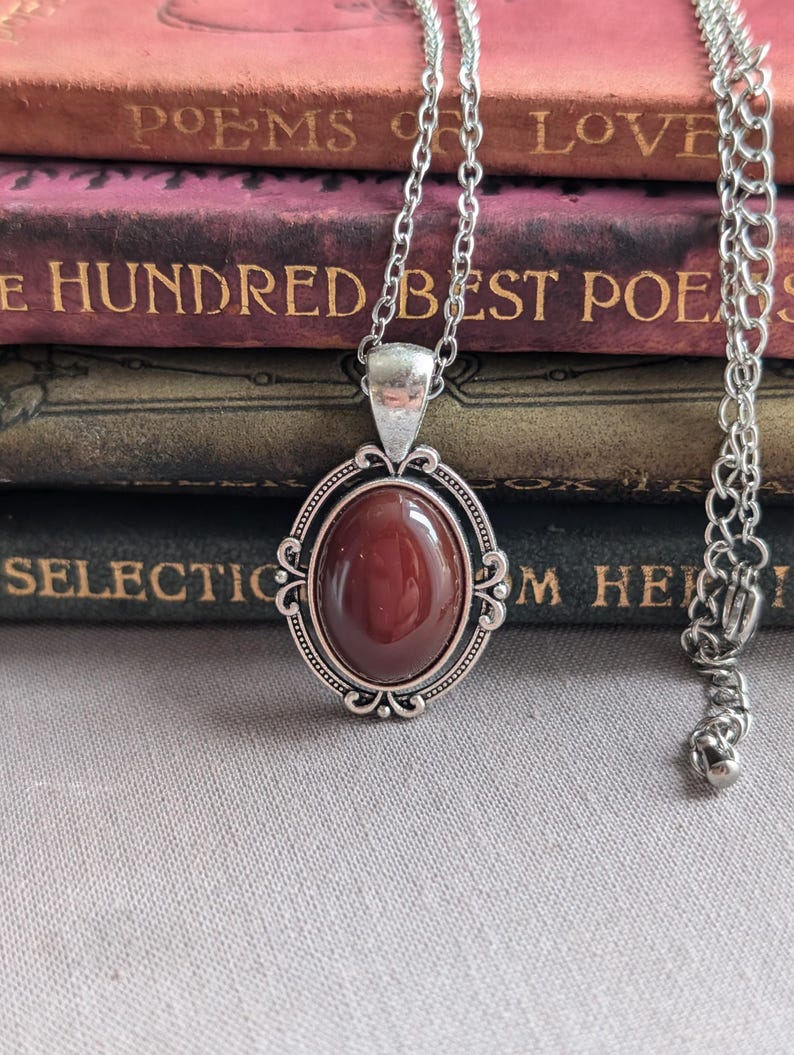 Blood Red Agate Crystal Necklace - Silver Flourish Pendant Setting on a stack of books