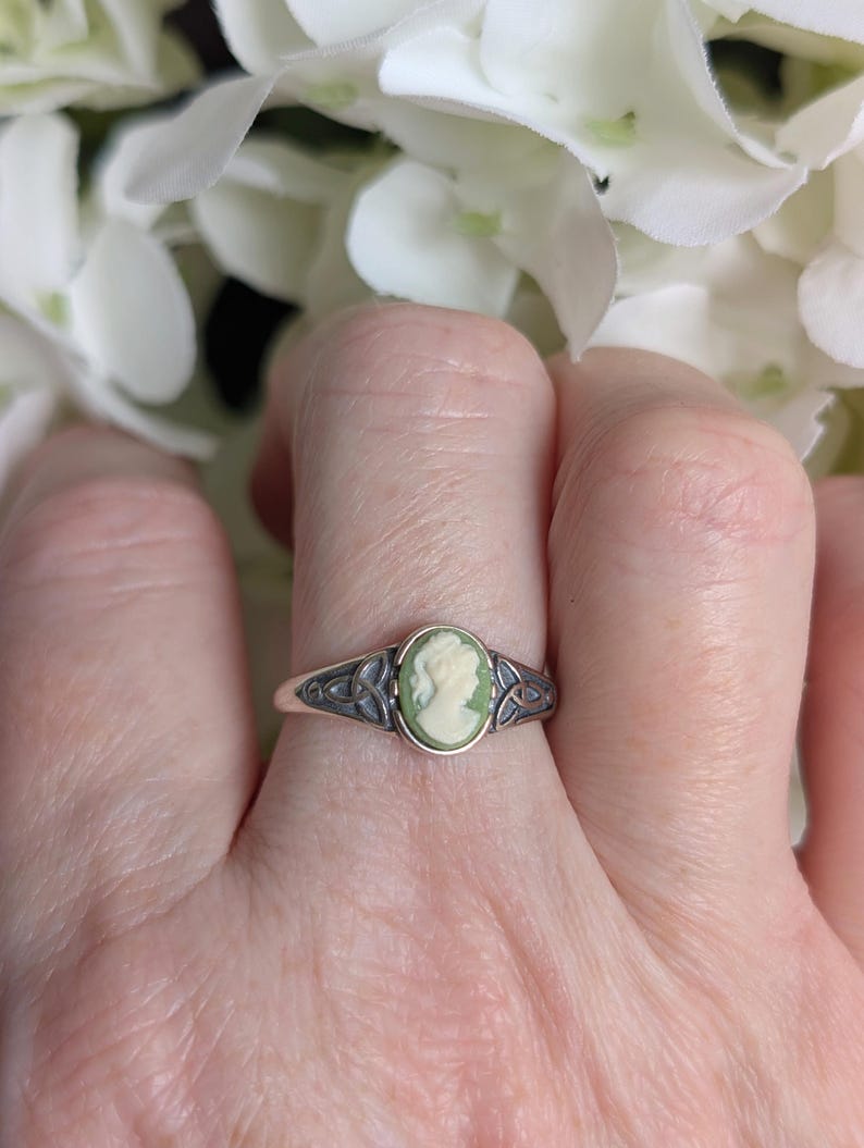 925 Sterling Silver Celtic Knot Cameo Ring - Heritage Style Jewelry with an ivory on green cameo on a finger against a white flower background