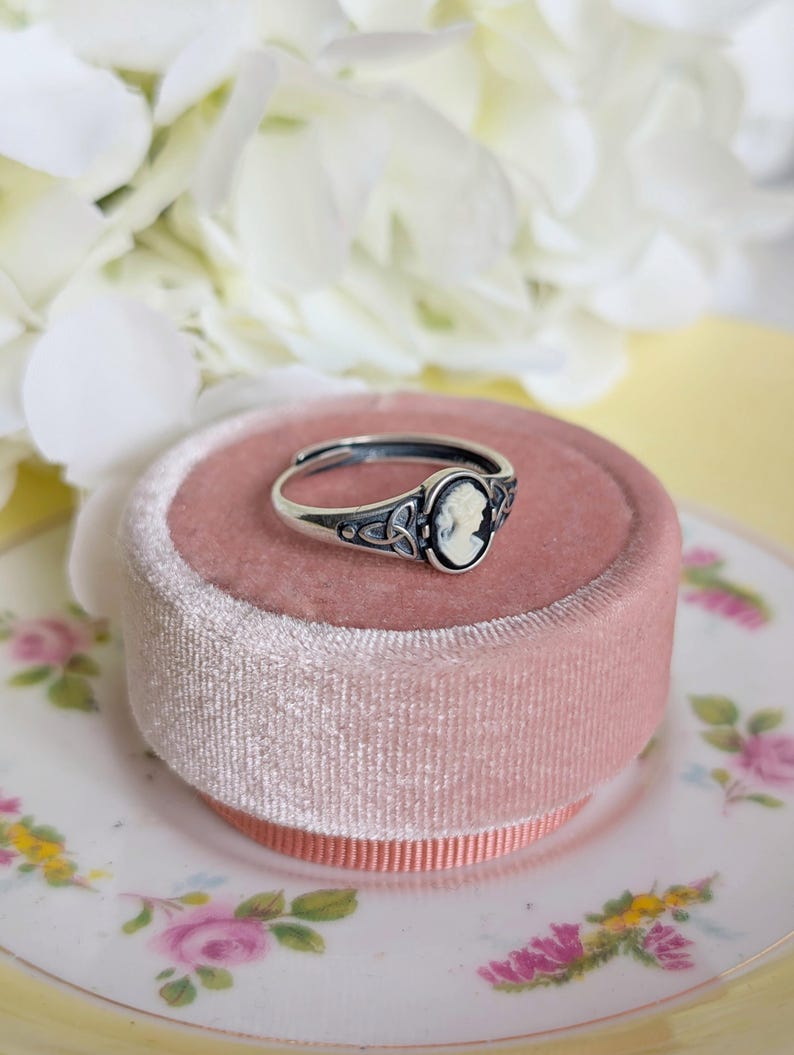 925 Sterling Silver Celtic Knot Cameo Ring - Heritage Style Jewelry with an ivory on black cameo on a pink velvet cushion with white flowers in the background