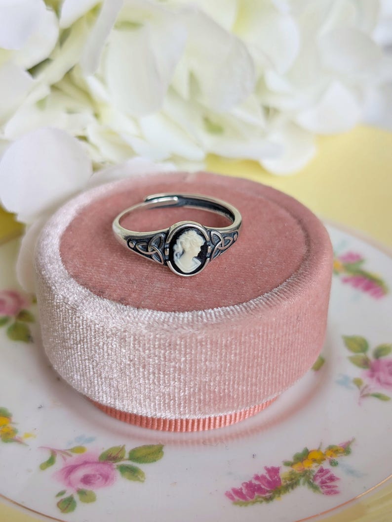 925 Sterling Silver Celtic Knot Cameo Ring - Heritage Style Jewelry with an ivory on black cameo on a pink velvet cushion, surrounded by white flowers.