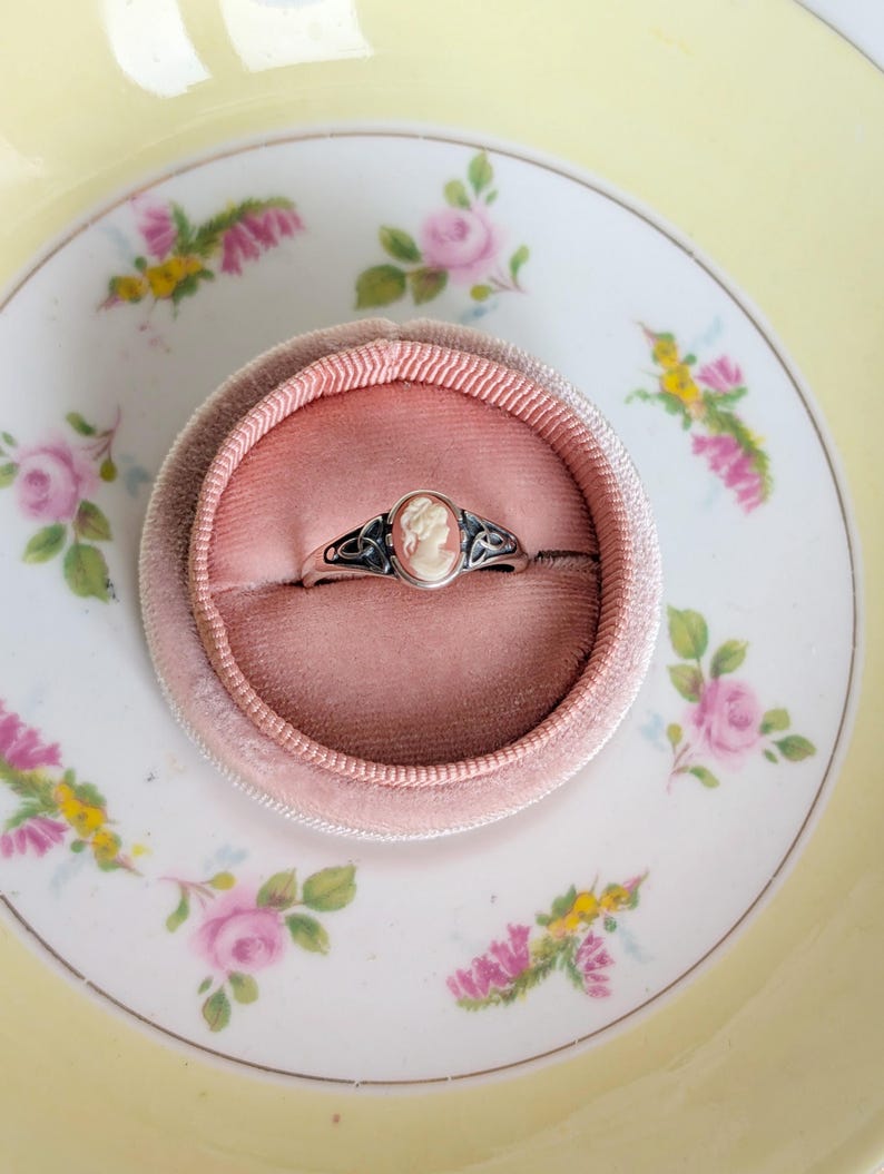925 Sterling Silver Celtic Knot Cameo Ring - Heritage Style Jewelry with an ivory on carnelian cameo in a pink cushion on a floral teacup