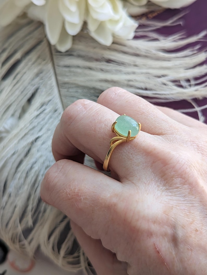 Hand wearing a Natural Green Aventurine Solitaire Ring - 18K Gold Vermeil over Sterling Silver - Handmade Gemstone Jewelry - Made in Toronto against a blurred floral background