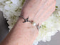 Hand wearing a Silver Swallow Bracelet with Glass Pearl and Toggle Clasp against a white floral background