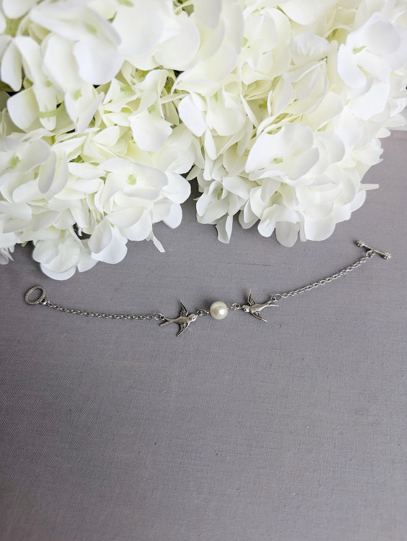 Silver Swallow Bracelet: Glass Pearl Bird Jewelry with Toggle Clasp on a gray surface with white flowers.