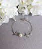 Silver Swallow Bracelet: Glass Pearl Bird Jewelry with Toggle Clasp on a gray surface with white flowers in the background