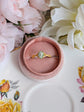 Matte gold cameo ring with single loop shoulder and green cameo detail in a pink velvet box surrounded by flowers