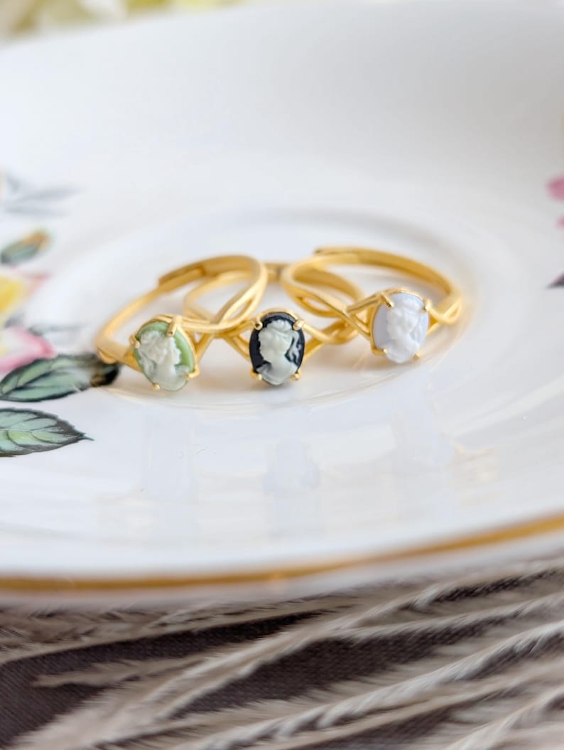 Three Matte gold cameo rings with single loop shoulder detail on a floral teacup.