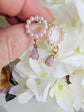 Handmade Pearl and Fire Opal earrings held by a hand with a floral background