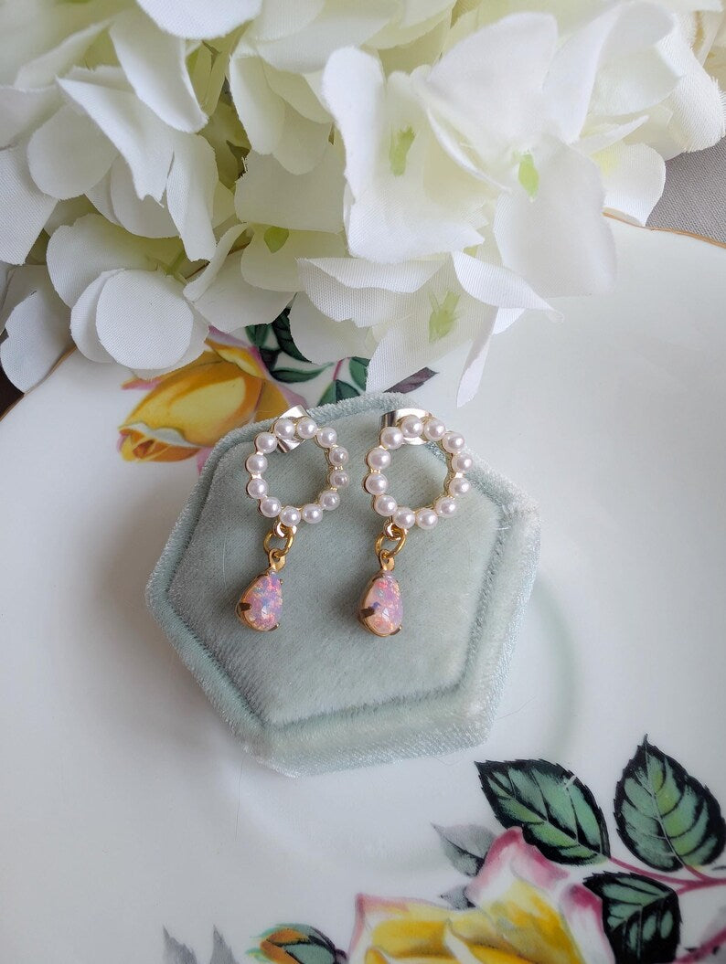 Handmade Pearl and Fire Opal earrings on a green hexagonal stand with floral background