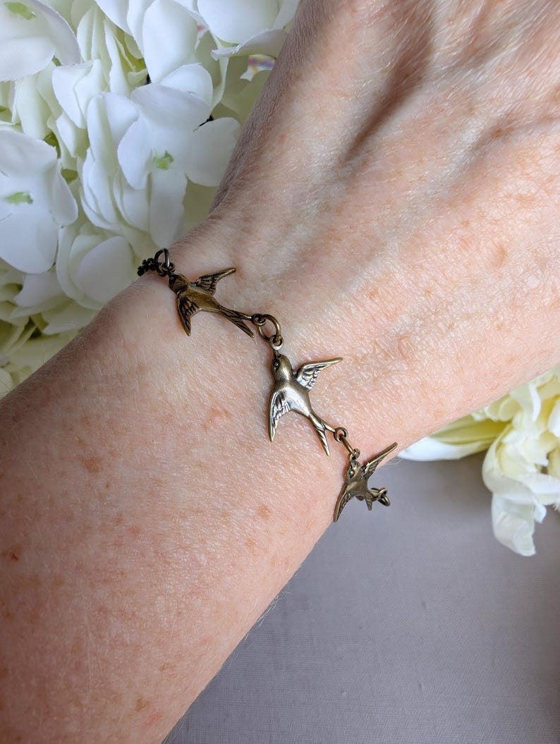 Bronze Swallow Bracelet on a wrist against a white floral background