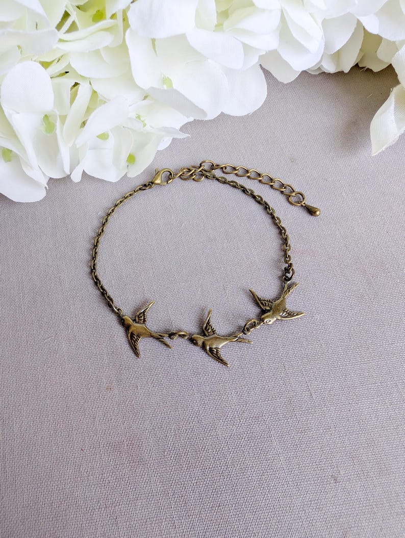 Bronze Swallow Bracelet, Dainty Trio of Flying Birds, Vintage Jewelry on a gray surface with white flowers in the background