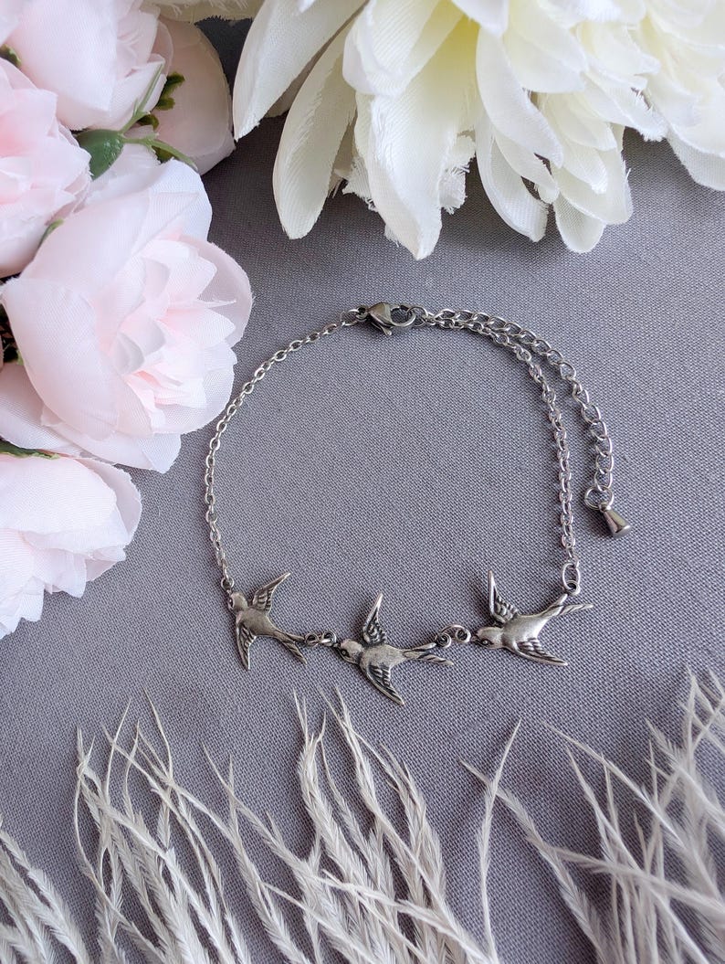 SIlver Swallow Bracelet, Dainty Trio of Flying Birds, Vintage Jewelry on a gray surface with pink and white flowers and dried grasses.