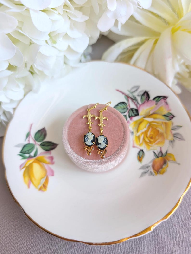 Handmade ivory on black cameo earrings with gold Fleur de Lis connectors and cognac Austrian crystals on a floral teacup.