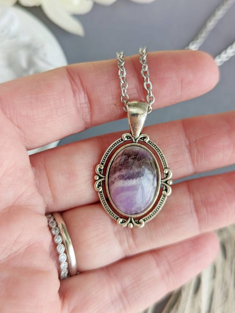 Purple Amethyst Crystal Necklace - Silver Flourish Pendant Setting held in a hand with a blurred background
