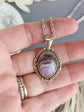 Purple Amethyst Crystal Necklace - Silver Flourish Pendant Setting held in a hand with a blurred background