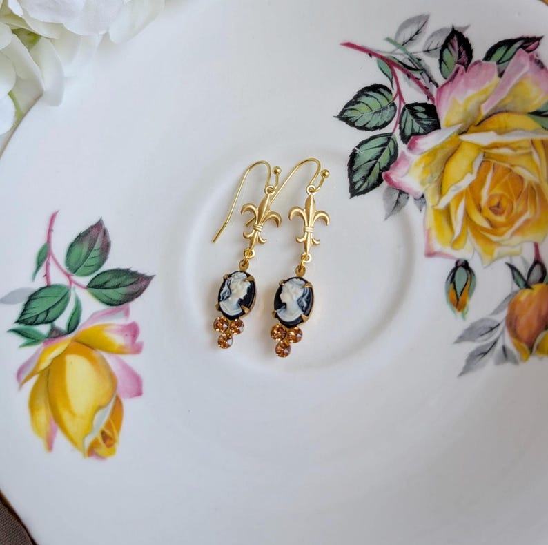 Handmade ivory on black cameo earrings with gold fleur de lis connectors and cognac Austrian crystals on a floral teacup.