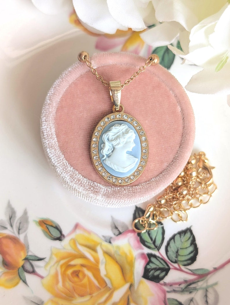 Handmade Gold Blue Lady Cameo Necklace with CZ Halo on Station Chain on a pink velvet cushion, floral background