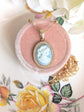 Handmade Gold Blue Lady Cameo Necklace with CZ Halo on Station Chain on a pink velvet cushion, floral background