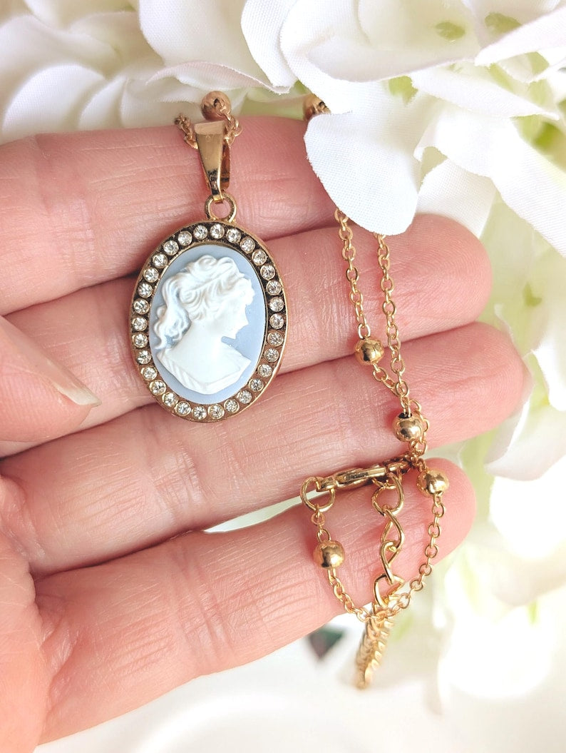 Handmade Gold Blue Lady Cameo Necklace with CZ Halo on Station Chain held in a hand against a floral background