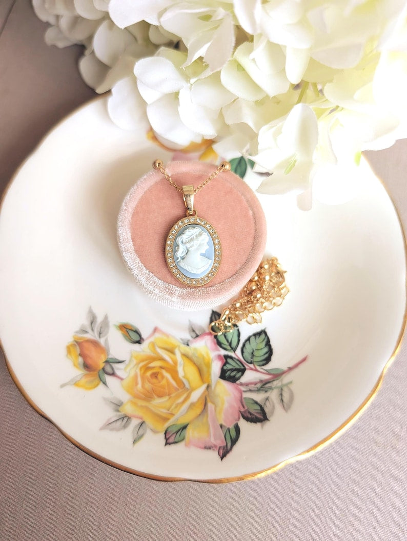 Handmade Gold Blue Lady Cameo Necklace with CZ Halo on Station Chain with a pink box on a decorative plate with floral design