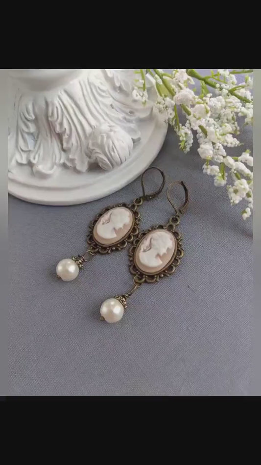 Pair of peach and white vintage lady cameo drop earrings with antiqued brass lace frames and glass pearl drops.
