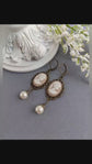 Pair of peach and white vintage lady cameo drop earrings with antiqued brass lace frames and glass pearl drops.
