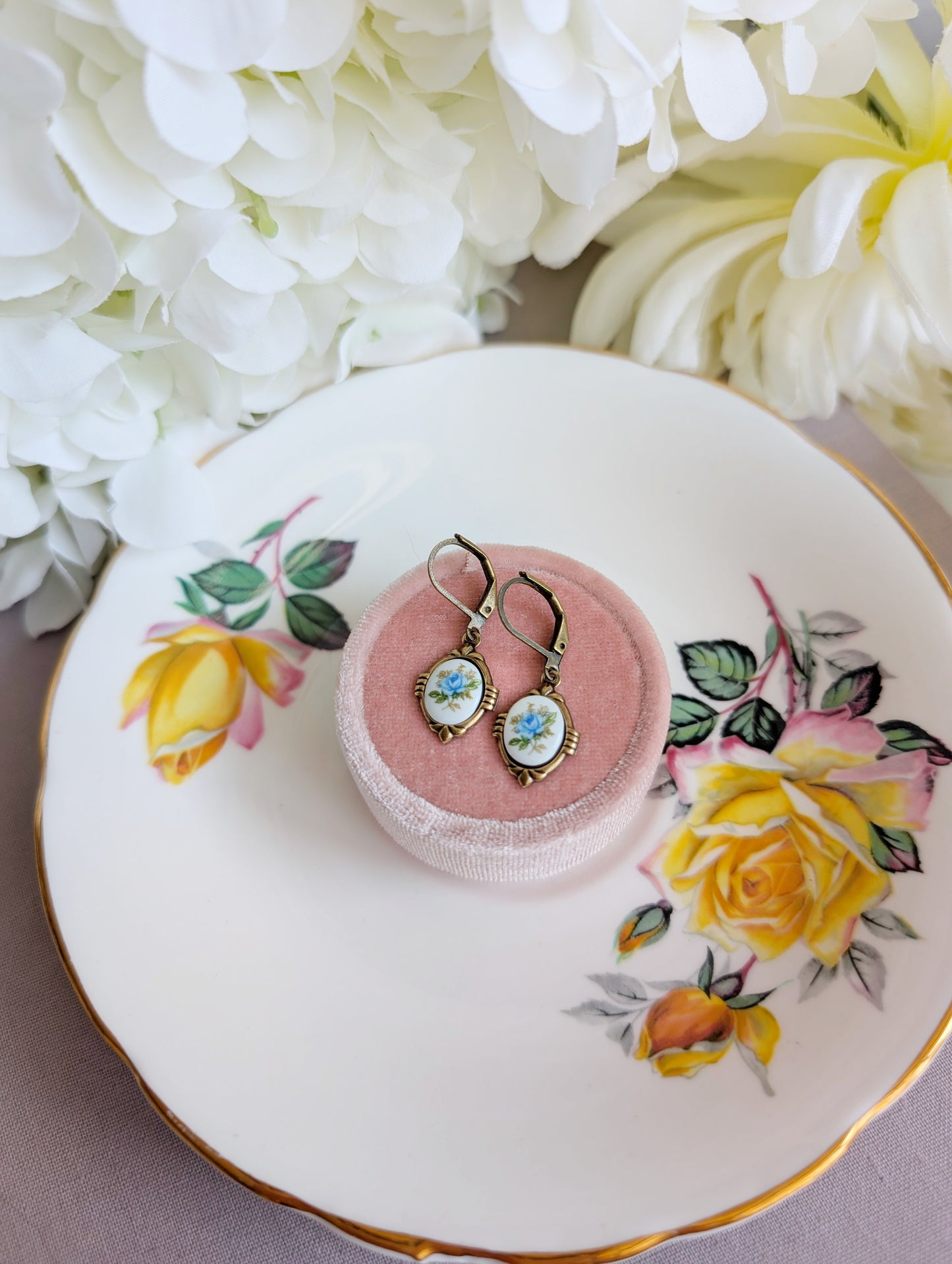 Blue Floral Porcelain Cabochon Earrings - Art Deco Frame - Victorian Style on a pink jewelry box with floral design on a decorative plate.