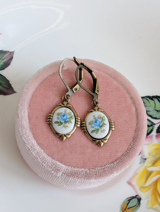 Blue Floral Porcelain Cabochon Earrings - Art Deco Frame - Victorian Style on a pink jewelry box with decorative leaves in the background